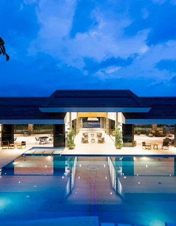 A luxurious outdoor pool with surrounding lounge areas, set against a modern building under a deep blue sky at twilight.