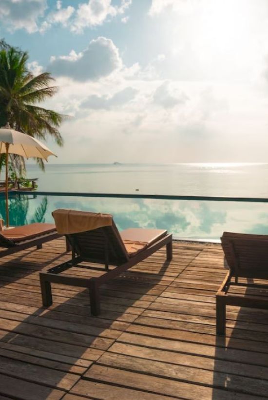 A tranquil poolside scene with lounge chairs, umbrellas, and a stunning ocean view under a partly cloudy sky.