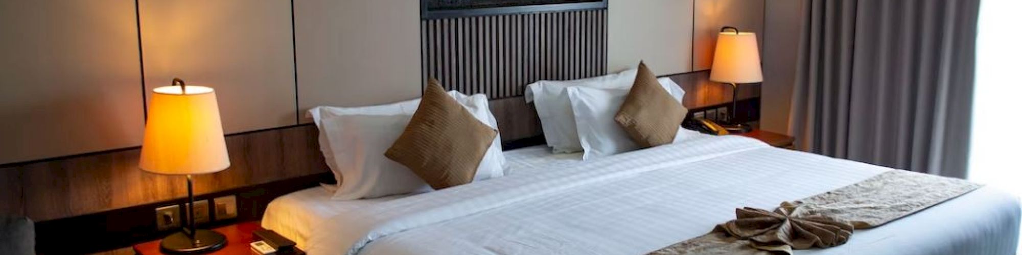 A cozy hotel room featuring a king-sized bed, two bedside lamps, and elegant decor, creating a warm and inviting atmosphere.