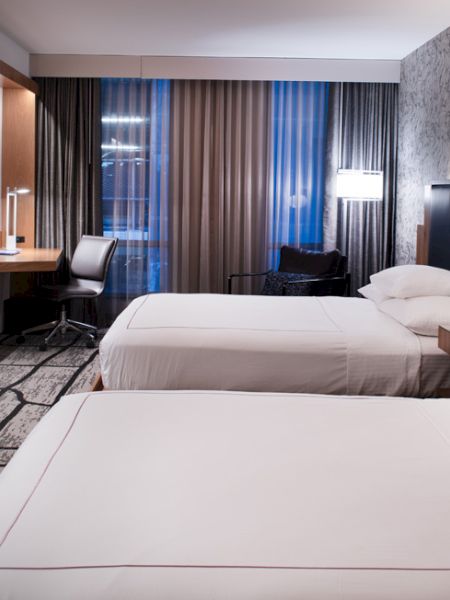 A modern hotel room with two beds, a wall-mounted TV, desk area, and decorative wallpaper accents.
