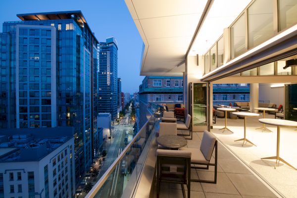 A modern rooftop terrace with tables and chairs overlooking a cityscape of tall buildings during twilight.