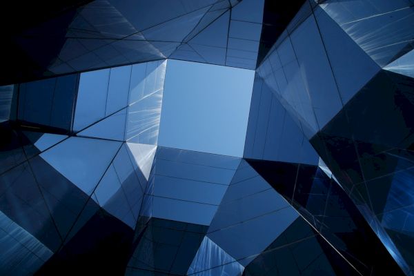 Geometric architectural structures with reflective glass, forming a pattern against the sky, viewed from below.