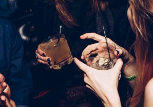 People are enjoying drinks and having a conversation in a lively social setting, with smiles and relaxed gestures.