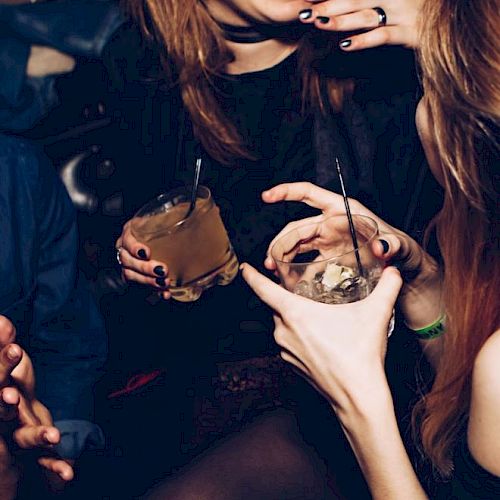 People are enjoying drinks and having a conversation in a lively social setting, with smiles and relaxed gestures.
