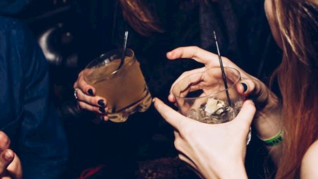 People are enjoying drinks and having a conversation in a lively social setting, with smiles and relaxed gestures.