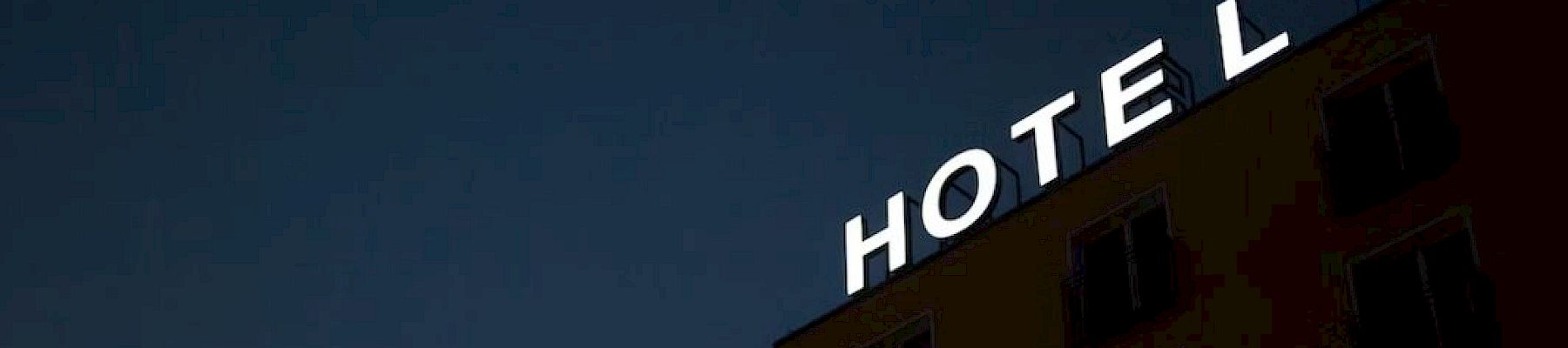 A building with a sign saying "HOTEL" at night, against a dark sky, with only partial view of the structure.