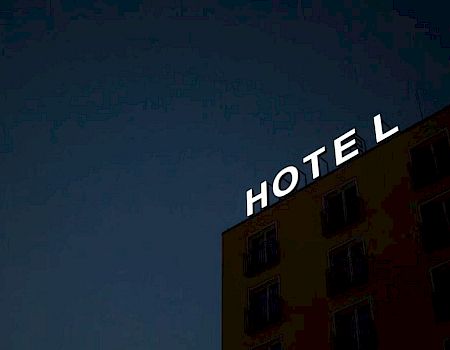 A building with a sign saying "HOTEL" at night, against a dark sky, with only partial view of the structure.
