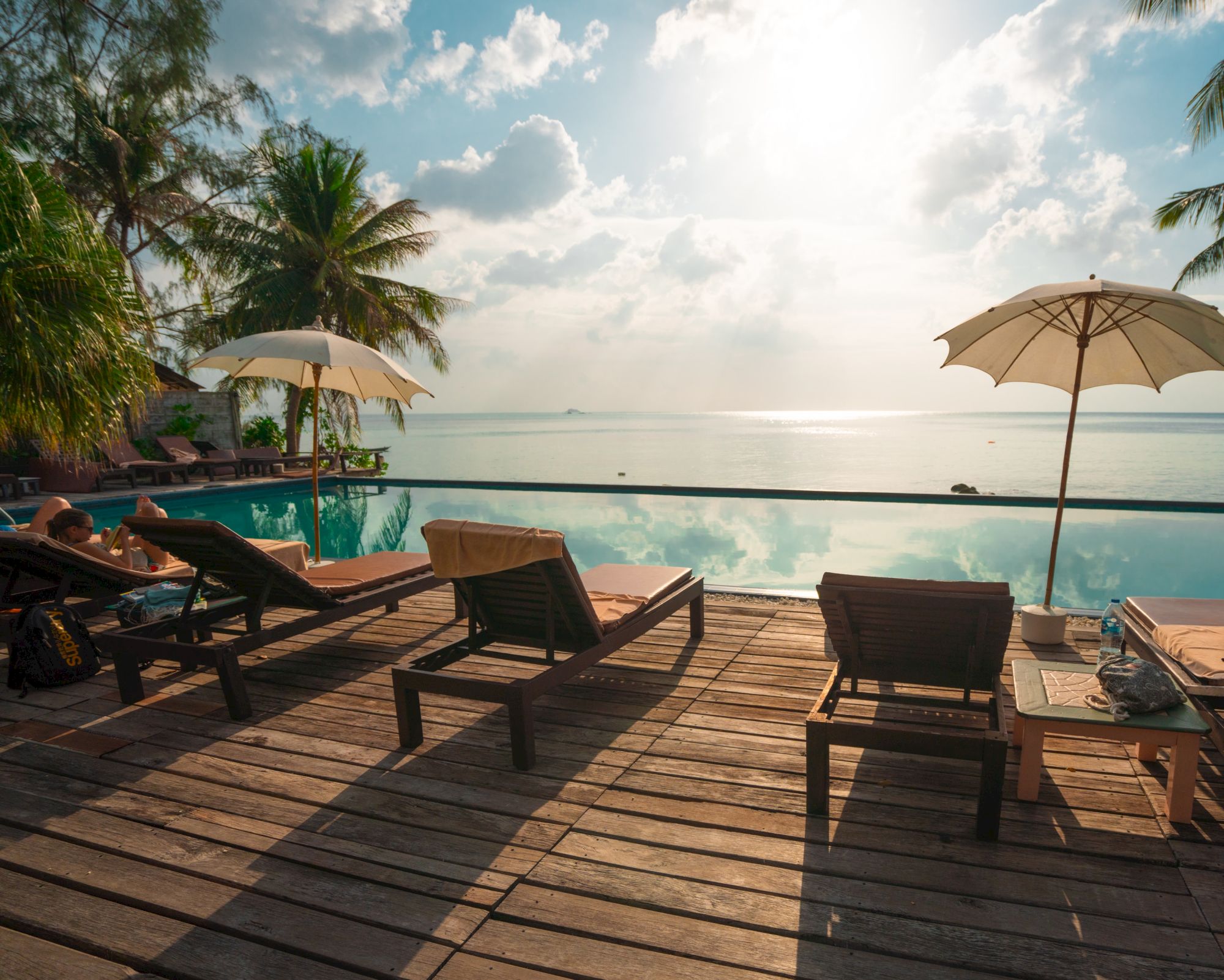 A serene beachside scene with lounge chairs, umbrellas, and a pool overlooking the ocean under a bright sky.