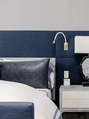 A modern bedroom with a navy headboard, neatly arranged bed, and a nightstand featuring a stylish lamp and decorative items.