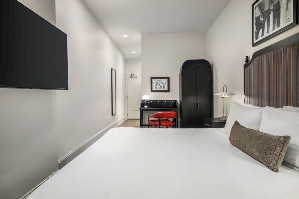 A modern hotel room with a large bed, wall-mounted TV, black furniture, and framed artwork. Simple and minimalistic design.