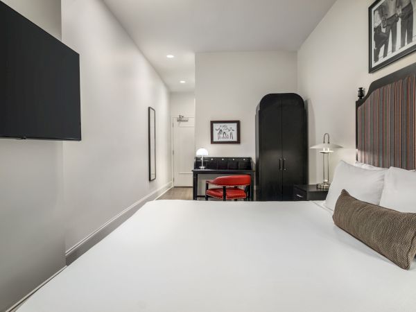 A modern hotel room with a large bed, wall-mounted TV, black furniture, and framed artwork. Simple and minimalistic design.