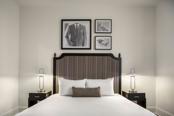 A neatly made bed with a striped headboard is flanked by two lamps. Above the bed, three framed artworks are displayed on the wall.