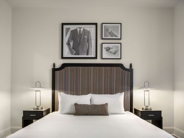 A neatly made bed with a striped headboard is flanked by two lamps. Above the bed, three framed artworks are displayed on the wall.