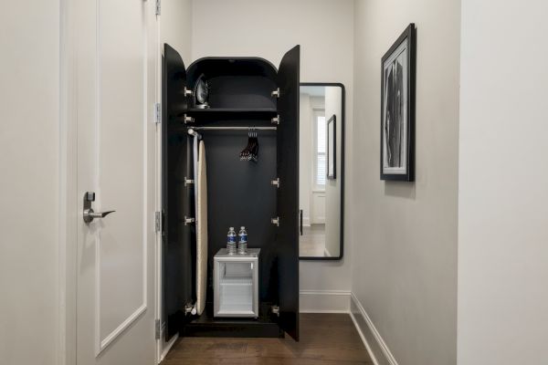 A small closet contains a clothing care system with hanging space and a compartment holding two water bottles, set in a narrow hallway.