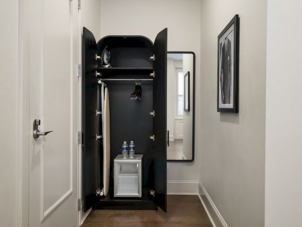 A small closet contains a clothing care system with hanging space and a compartment holding two water bottles, set in a narrow hallway.