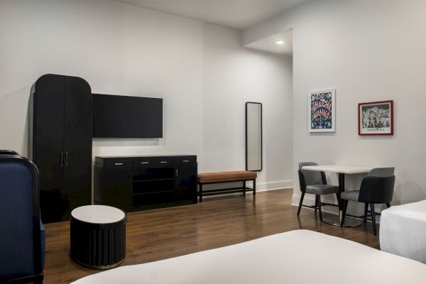 A modern room with a TV, table, chairs, wardrobe, and wall art. Features wooden flooring and minimalist decor.
