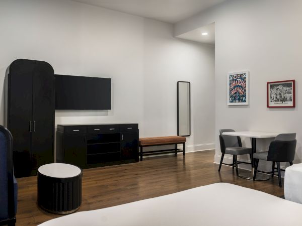 A modern room with a TV, table, chairs, wardrobe, and wall art. Features wooden flooring and minimalist decor.