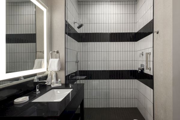 Modern bathroom with a walk-in shower, black and white tiles, a large mirror, and a sleek black countertop with a sink.