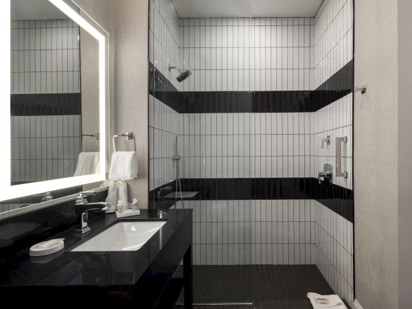 Modern bathroom with a walk-in shower, black and white tiles, a large mirror, and a sleek black countertop with a sink.