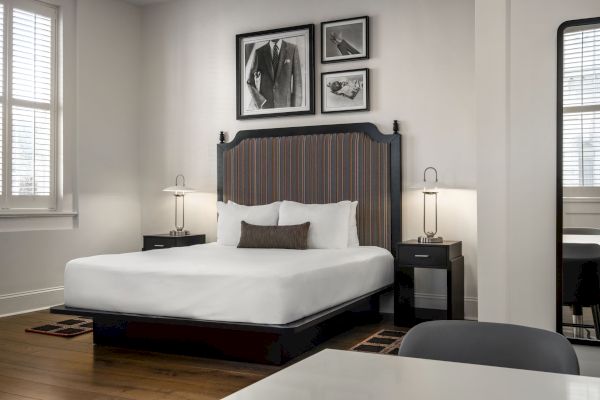 A modern bedroom with a large bed, two side tables, and lamps. Black-and-white photos above the bed and a tall mirror on the right.