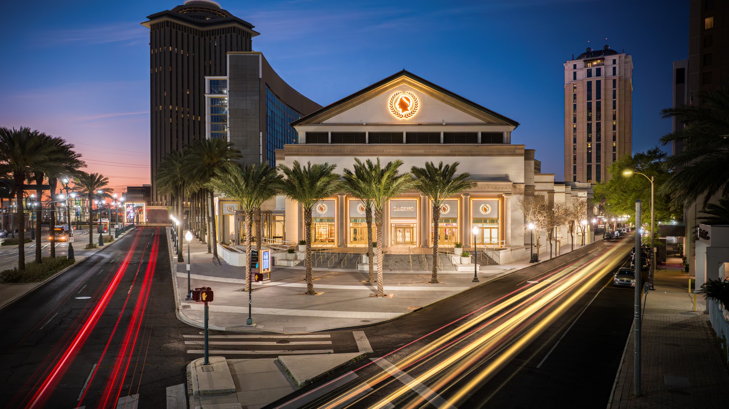 A hotel exterior at dusk with palm trees and streetlights.