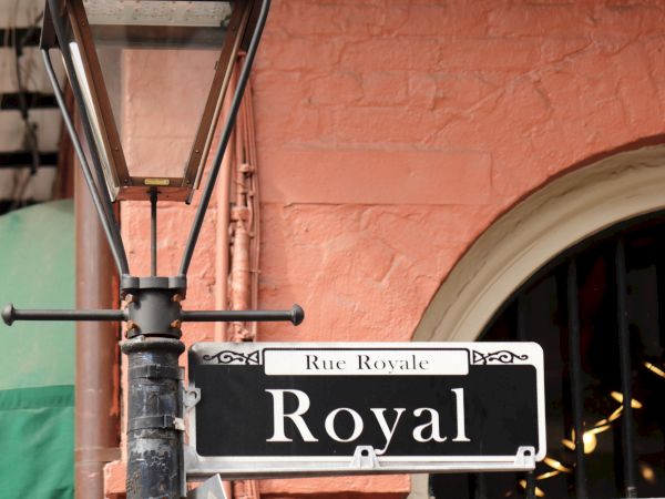 A street sign for "Royal" next to a vintage lamp post against a pink brick wall.