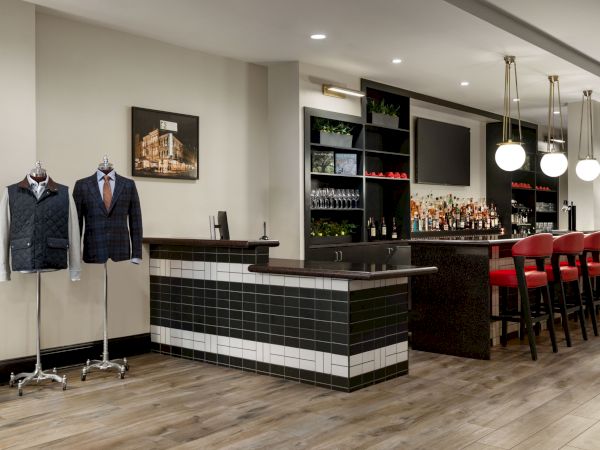 A stylish bar with red stools, mannequins in suits, modern lighting, and wooden flooring, creating a chic and inviting atmosphere.