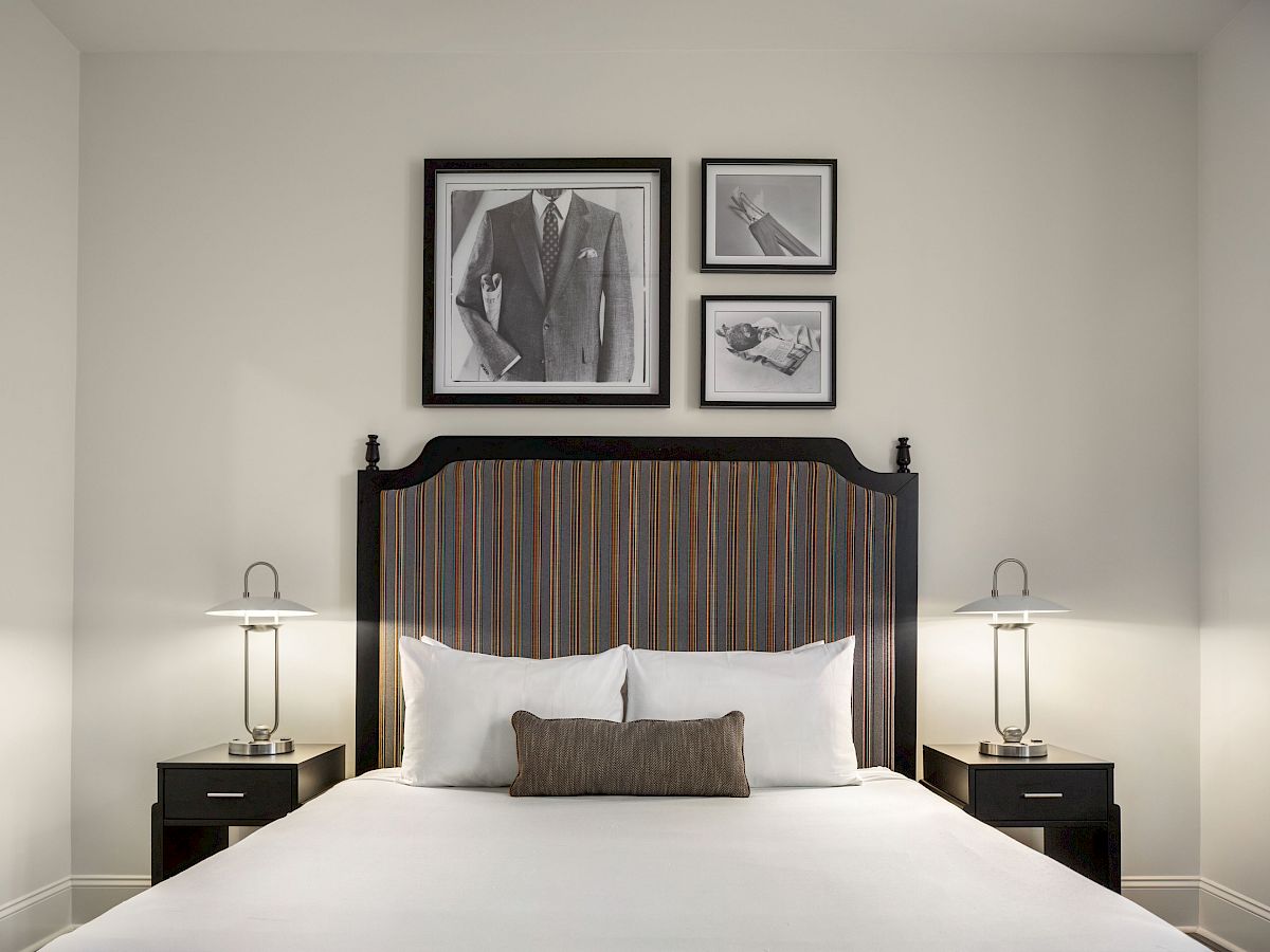 A neatly made bed with a dark headboard, flanked by two lamps, and three black and white framed photos above.