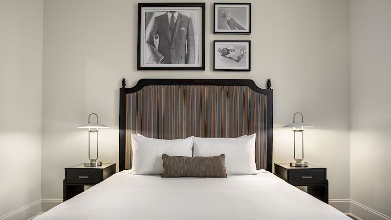 A neatly made bed with a striped headboard, two nightstands with lamps, and three framed pictures above the bed.