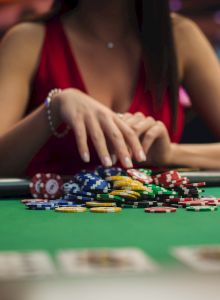 A person in a red outfit is handling poker chips on a casino table with playing cards in view.
