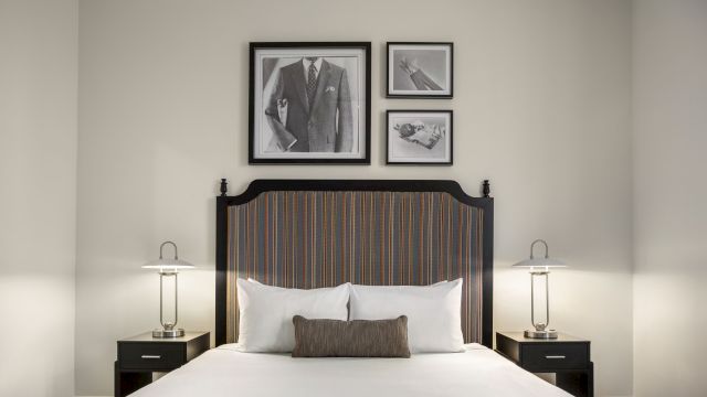 A neatly made bed with a striped headboard, two nightstands with lamps, and three framed pictures on the wall above the bed.