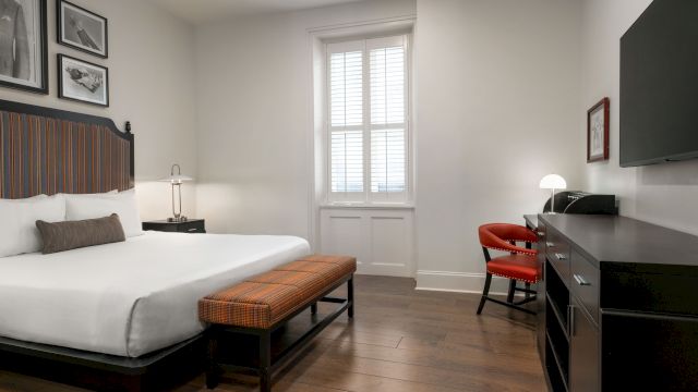 A wide view of a hotel room with a bed, TV, chair, and window
