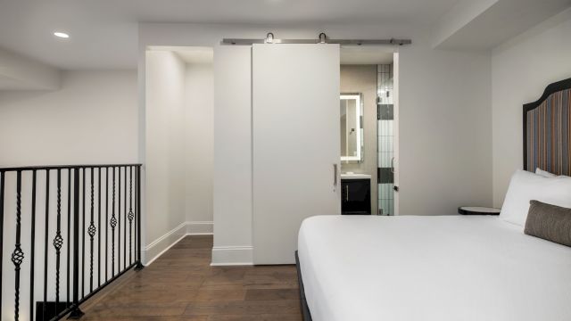 A wide view of a hotel room with a bed, a bathroom door, and a railing.