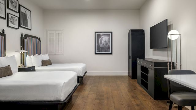 A hotel room with two beds, a desk, and a TV on the wall.