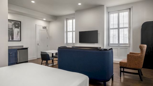 A wide view of a hotel room with a bed, TV, chair, table, and mini_fridge.
