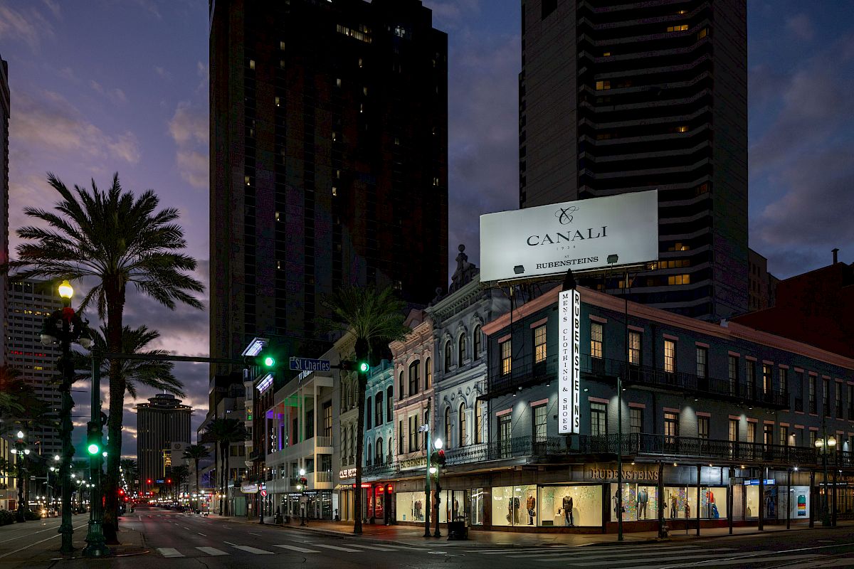 Street scene at dusk with lit palm trees, a billboard, and historic buildings. Urban and calm atmosphere.