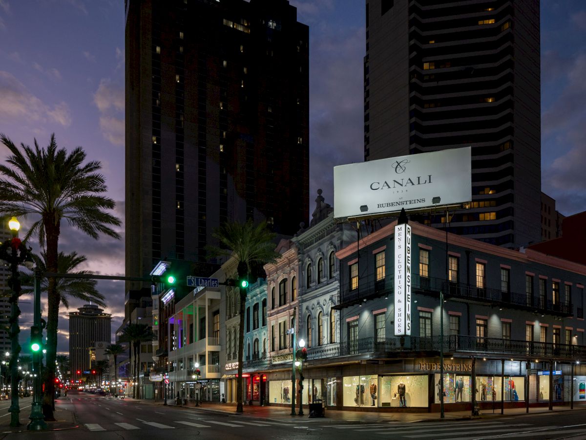 Street scene at dusk with lit palm trees, a billboard, and historic buildings. Urban and calm atmosphere.