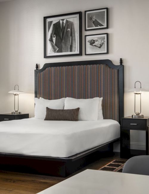 A modern bedroom with a double bed, two side tables, and lamps. Three black-and-white pictures hang above the bed.