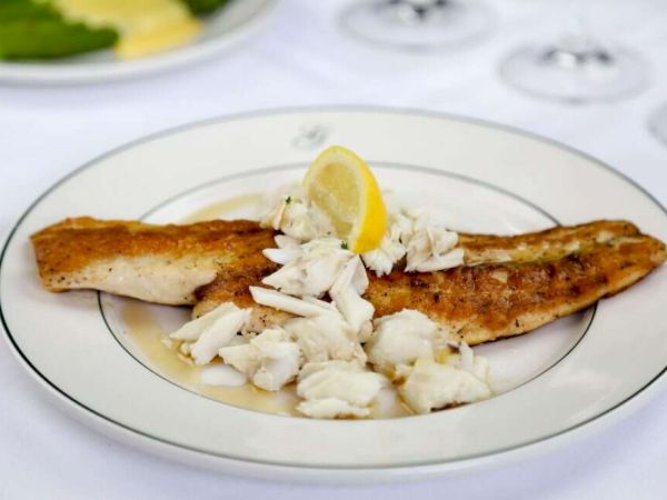 A plate of grilled fish topped with crab meat and a lemon wedge.