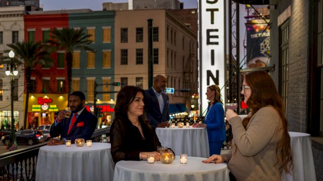 People sitting at tables with lit candles on a balcony overlooking a city street