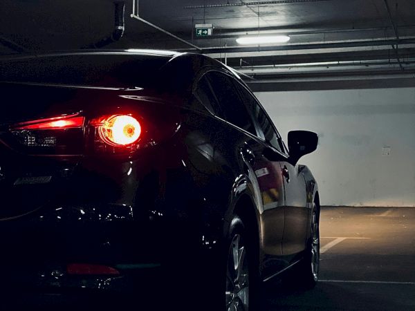 A car with red taillights illuminated is parked in a dimly lit underground parking garage.