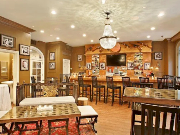 A cozy dining room with warm brown walls, wood furniture, a chandelier, and framed photos; tables and chairs arranged for casual meals.