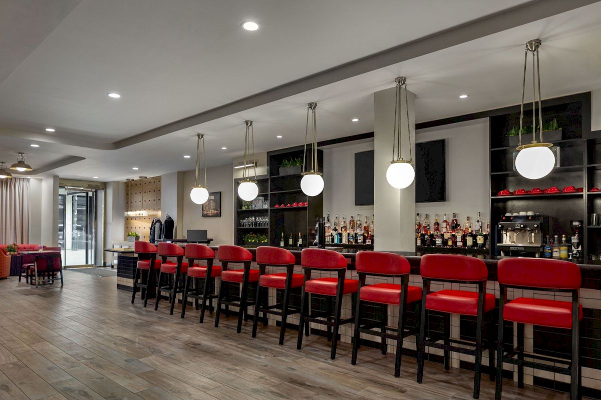 A wide view of a bar with red stools and a counter with shelves of alcohol bottles.