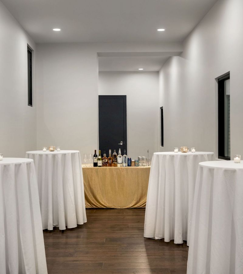 A bar area with white tables, a gold tablecloth, and bottles and glasses on display.