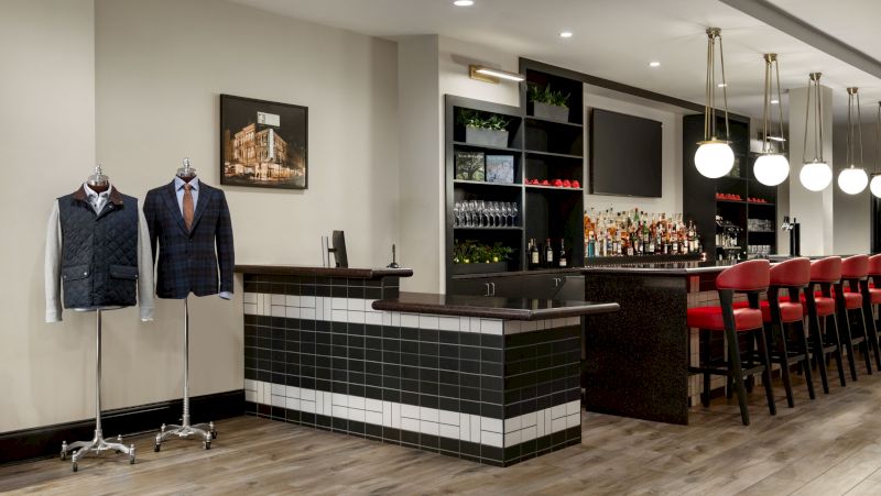 A bar with a black and white tile counter, red chairs, and mannequins dressed in suits.