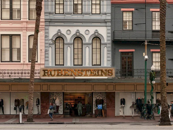Rubenstein's storefront with pastel historic buildings, shoppers outside, and palm trees lining the sidewalk in front of the boutique.