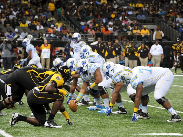 American football at the line of scrimmage, players in helmets and jerseys crowd around the ball during a tense play.
