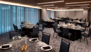 The image shows an elegant banquet hall with circular tables set for an event, featuring black chairs and soft lighting.
