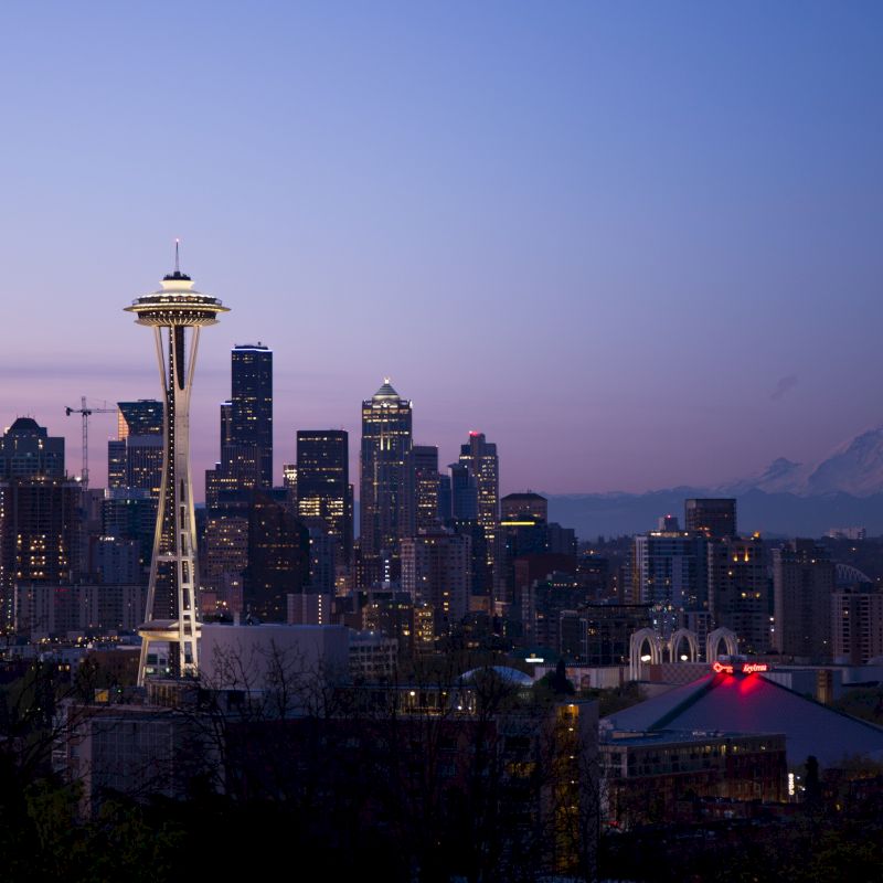 Seattle skyline at dusk with the Space Needle and Mount Rainier in the background, under a gently fading blue and pink sky.