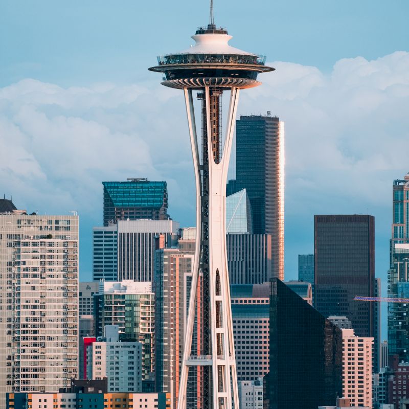 The image features the Space Needle with surrounding skyscrapers against a backdrop of clouds and blue sky, capturing an iconic cityscape.